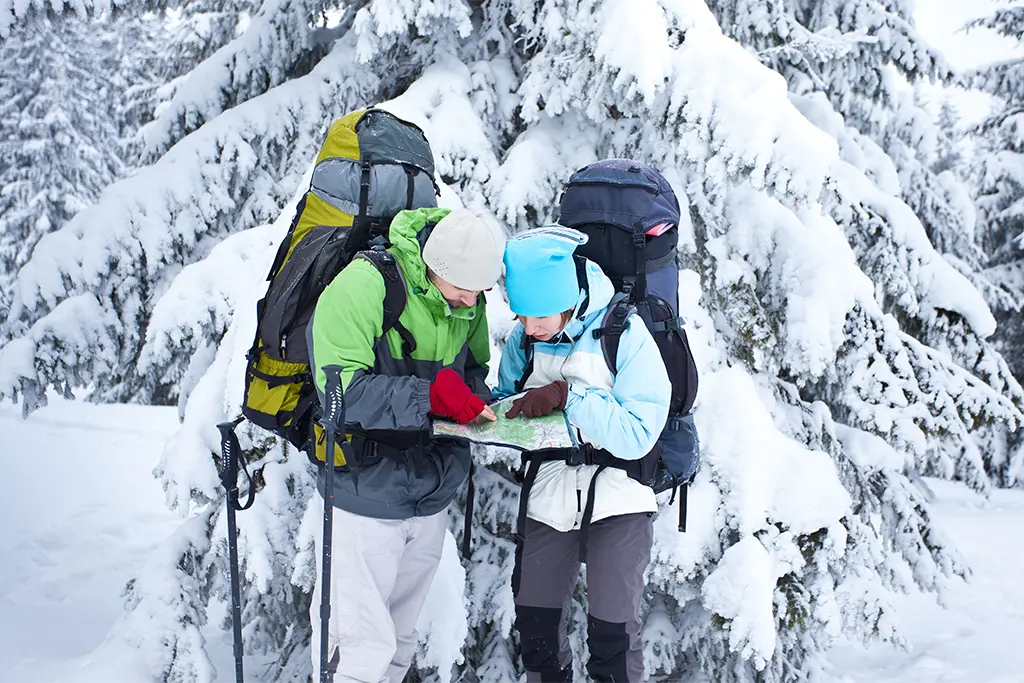 Zwei Teilnehmer mit Schneeschuhen und Karte bei einem Teambuilding-Winterevent in Bad Herrenalb (Schwarzwald). Die Teilnehmer tragen einen Rucksack mit Teamequipment für ein Winter- Survival-Teamevent im Rahmen eines winterlichen Manager-Trainings (Leadership).