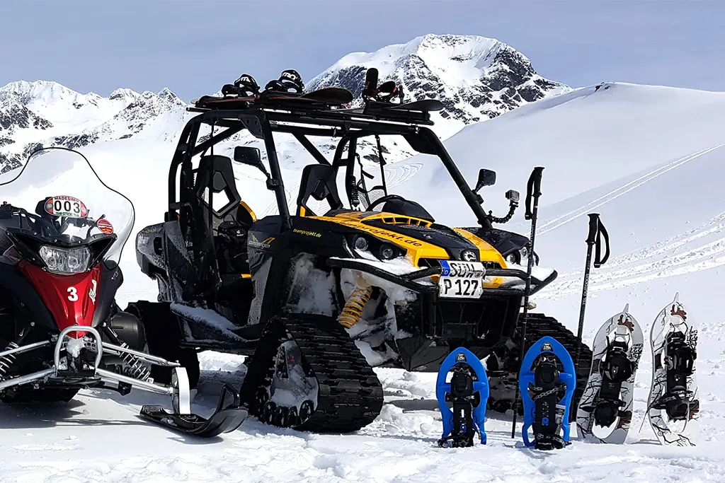 Quad und Motorschlitten im Schnee mit Schneeschuhen im Vordergrund im Rahmen eines Schnee-Teamevents in Tirol