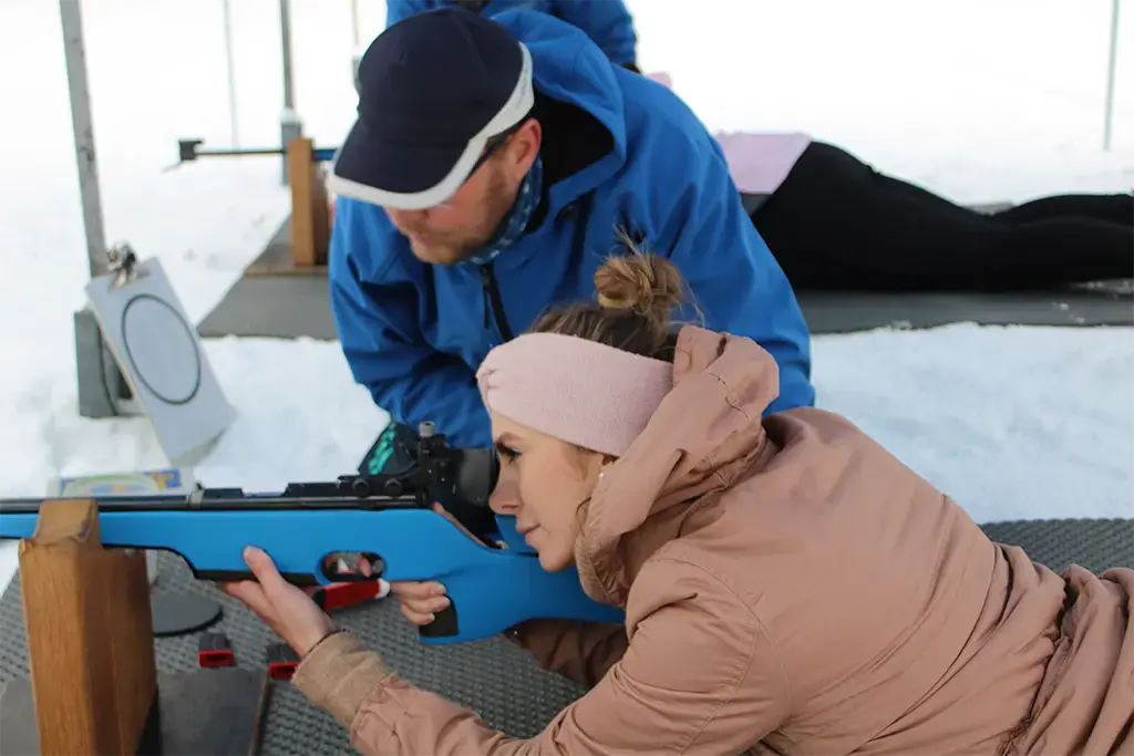 Biathlon Element beim Winterevent von team projekt, Teilnehmerin zielt mit dem Luftgewehr als Teil eines Firmen Incentives mit Schneeschuhwandern und Teambuilding Programm