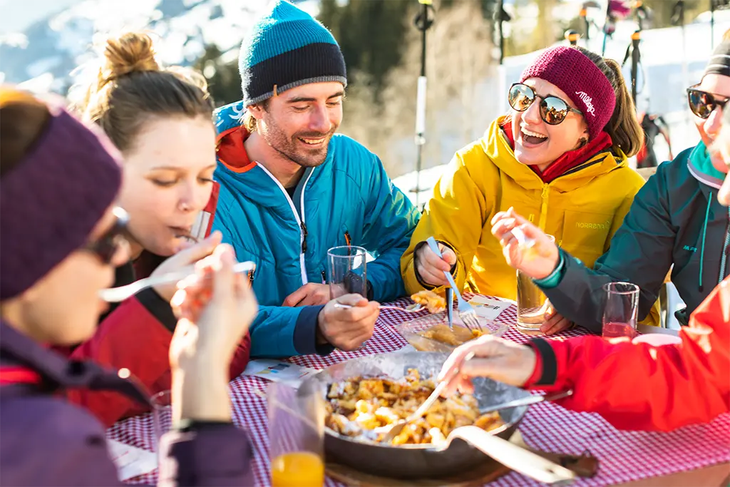 Teilnehmer genießen gemeinsam ein Outdoor Essen in den Alpen, kulinarisches Rahmenprogramm bei einem Winterevent und Corporate Incentive von team projekt