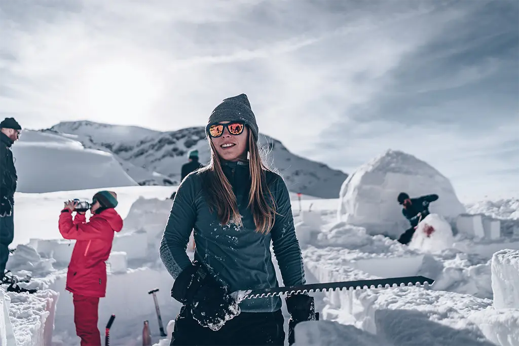 Winterevent-Teilnehmerin mit einer Iglublocksäge bei einem Iglubau-Teamevent im Schnee im Allgäu