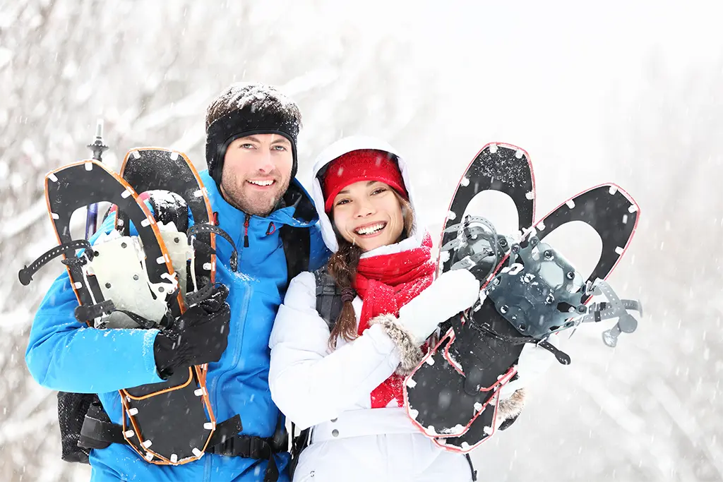 Zwei Teilnehmer mit Schneeschuhen die glücklich sind und das Schneeschuhevent in Reit im Winkl im Chiemgau genießen. Die Teilnehmer tragen Schneeschuhe von der Schneeschuhvermietung von team projekt.
