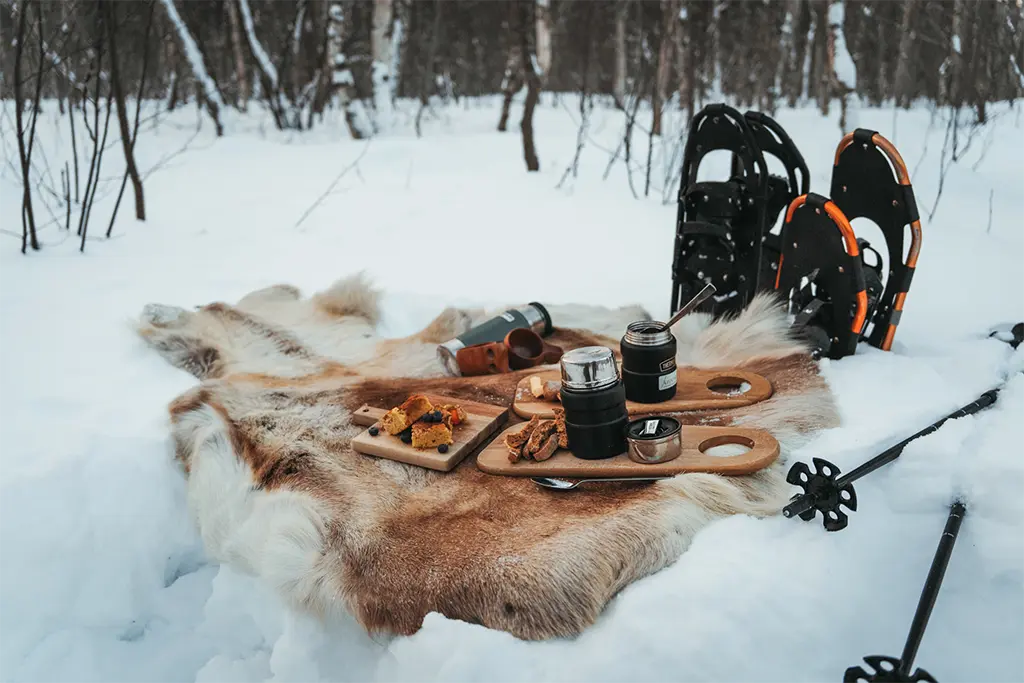 Winter-Picknick auf Rentiertfellen bei einem Winter-Incentive in Schwedisch-Lappland mit Schneeschuhen im Hintergrund. Geplant und organisiert über die Incentiveagentur team projekt.