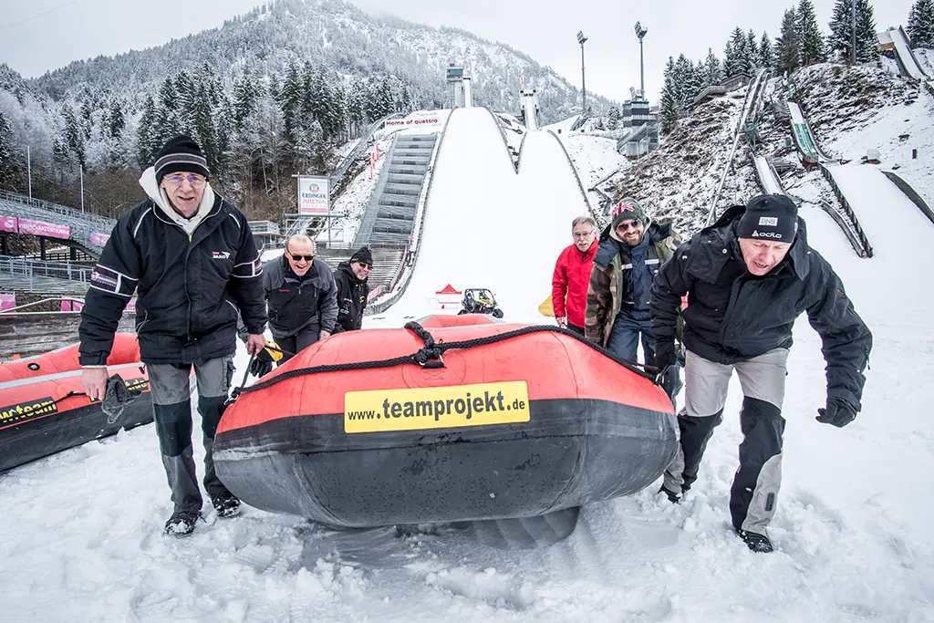 Teilnehmer ziehen ein Snow Rafting Boot im Schnee, actionreiches Winterevent von team projekt als Incentive Programm für Unternehmen und Gruppen