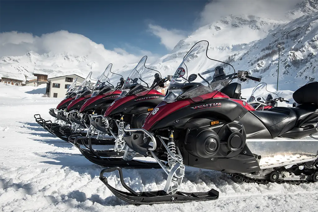 Fünf Skidoos bei einer  Motorschlittensafari in den Italienischen Alpen in Italien als Teil eines Winter-Teamevents im Schnee. 