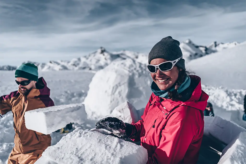 Zwei Teilnehmer beim Iglubau bei einem Teamevent im Schnee in Bad Reichenhall. Die Teilnehmerin lächelt und genießt das Winter Teambuildingevent