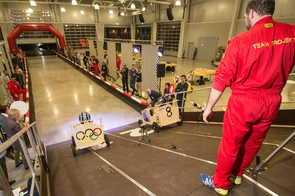 Eine Seifenkistenrampe mit einem Teamtrainer auf der Rampe der bei einem Seifenkistenrennen in Karlsruhe das Seifenkistenevent betreut. Auf dem Bild sieht man auch eine große Racingbahn mit aufblasbarem Zielbogen.