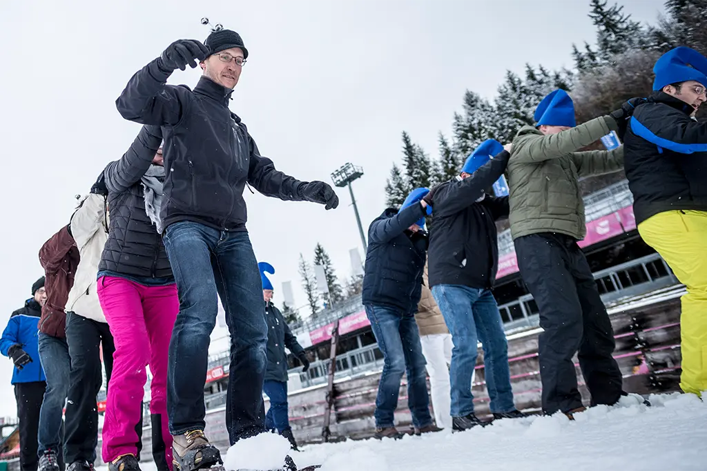 Zwei Winter Eventgruppen auf Riesenskiern bei einer winterlichen Teamolympiade im Schnee in Berchtesgaden. Die Teilnehmer lachen und haben bei dem Firmen Schneeevent viel Spaß