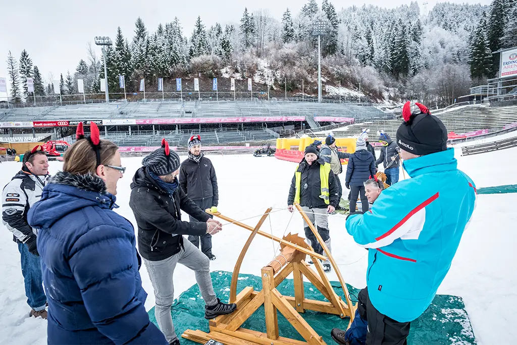 Incentive Teilnehmer im Winter die rund um ein Schneeball Katapult stehen und am Katapult mit Schneebällen schießen. Das Schneeball-Katapult ist Teil einer  Winterteamolympiade bei einem Teambuildingevent