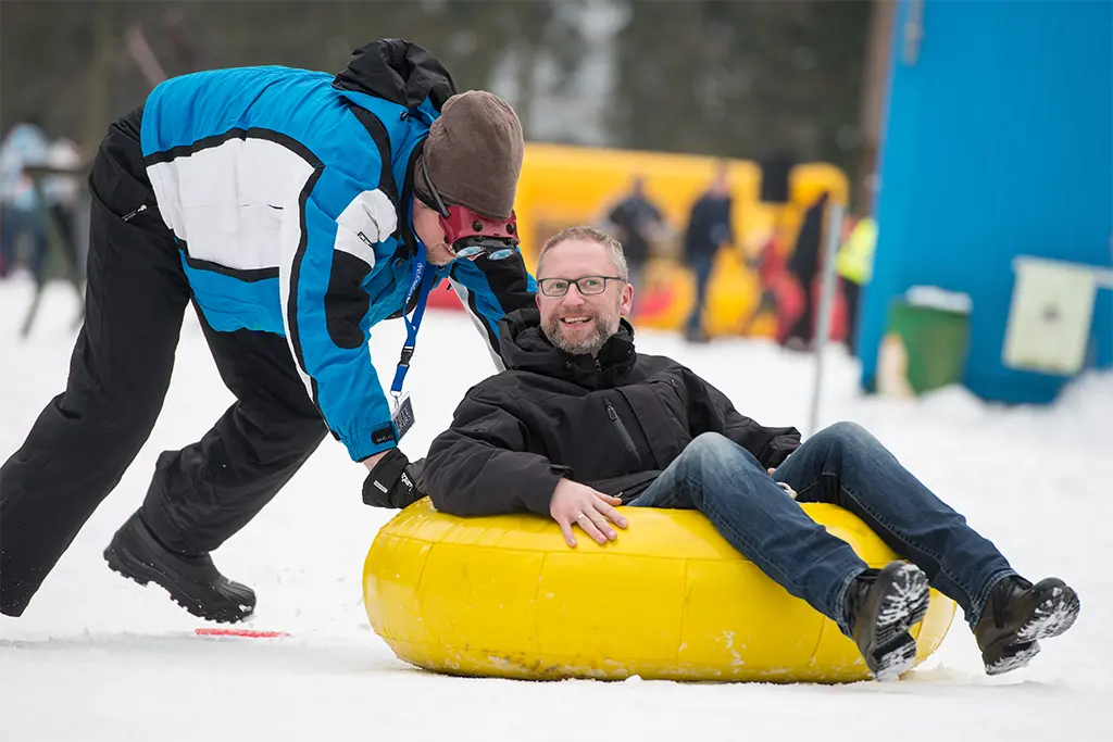 Ein Teilnehmer wird auf einem Snowtube durch einen  Snowtubing-Parcours geschoben und lacht dabei. Die Aufnahme entstand bei einem Teamevent auf Schloss Elmau