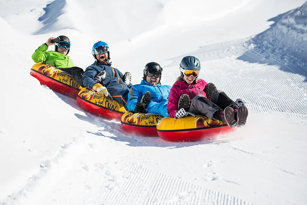 Gruppe mit vier Teilnehmern auf 4 Snowtubes bei einer rasanten Abfahrt im Zillertal als Teil eines Winterteamevents in Österreich. Die Teilnehmer bilden bei dem Snowtubing eine Kette und sind von der Winterincentivereise beeindruckt