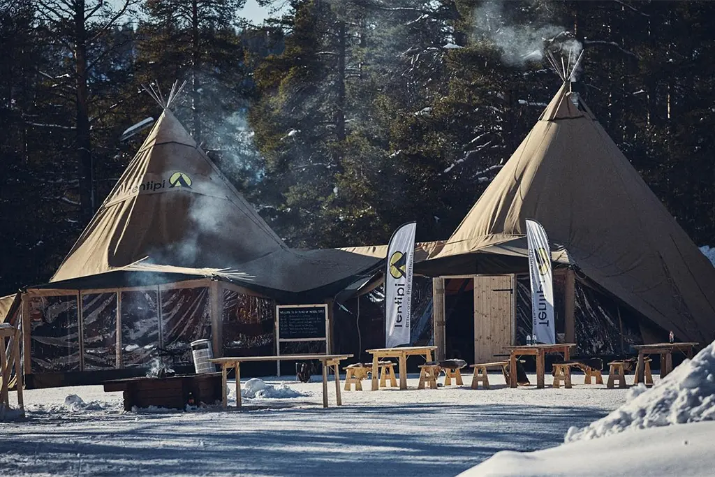 Ein Tagungszelt/Tagungstipi mit skandinavischen Eventtipis im Winter bei einem Kick Off Event im Schnee. Aus dem beheizten Eventtipis steigt Rauch aus dem Kamin. Das Foto wurde als Teil einer Outdoortagung im Winter gemacht.