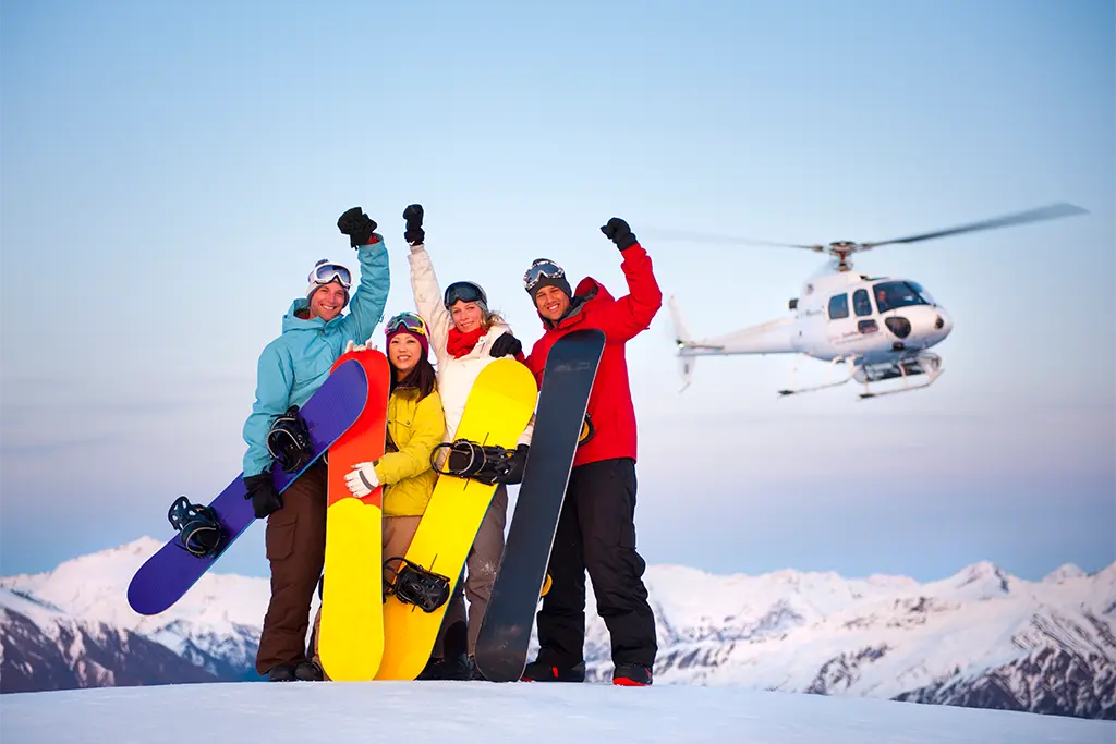 Eine Gruppe mit Snowboards und einem Helikopter im Hintergrund winkt und ist von der Incentivereise in Österreich begeistert. Das Winter Incentive hat team projekt durchgeführt