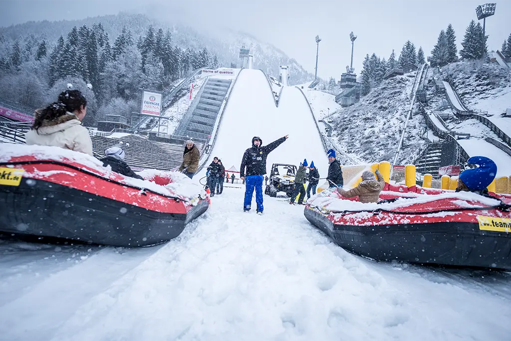Teilnehmer eines Teambuildingevents in Oberstdorf welche zwei Snowrafts bei einem Snowrafting Teamevent ziehen.