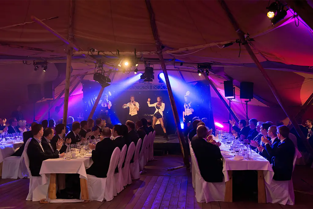 Eine Weihnachtsfeier in einem Eventtipi mit einer Showgruppe auf der Eventbühne bei einem Firmenevent. Das Eventzelt ist festlich dekoriert und bietet die perfekte Kulisse für eine Xmas Party