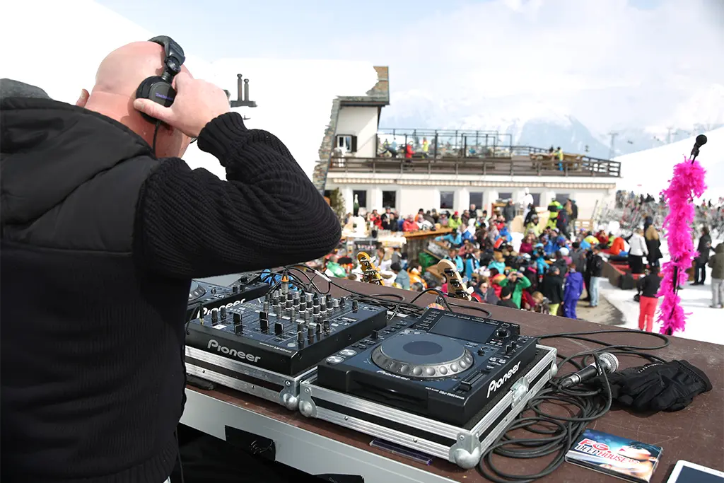 Ein DJ der bei einer großen AprésSki-Party Musik auf einer Eventlocation im Schnee Musik auflegt. Die Teilnehmer des  AprésSki-Events tanzen und feiern. Die Veranstaltung wurde von der Incentiveagentur die Erlebniscompany produziert.