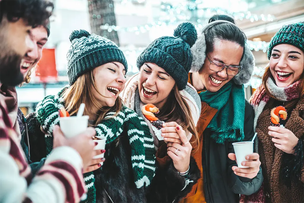 5 junge Leute mit beim Glühweintrinken als Teil einer Glühwein-Teamrally in Heidelberg. Die Teilnehmer lachen und sind von dem Winterrally Event begeistert.