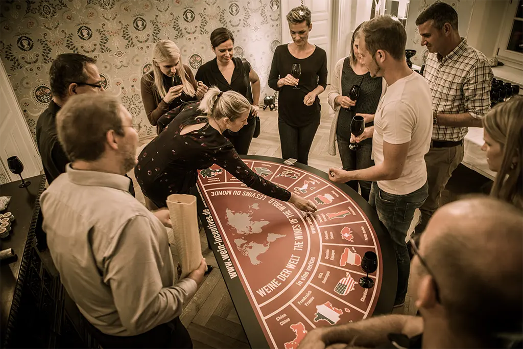 Über 10 Teilnehmer bei einem Weincasinoevent als Teil einer Weihnachtsfeier in Deidesheim. Eine Teilnehmerin des Firmenevents setzt an einem Weinpoker-Tisch Jetons und versucht bei dem Weinevent die richtigen Weine zu erraten.