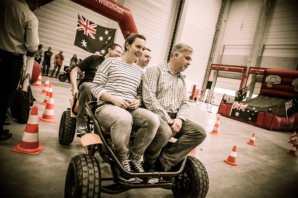 4 Firmeneventteilnehmer auf einem 4erKettcar, die einen Kettcarparcours bei einem Indoorteamevent befahren. Das Bild wurde bei einem Teamevent für ein Azubi-Event in Worms gemacht. Die Kettcars wurden bei der Livemarketing Agentur team projekt gebucht